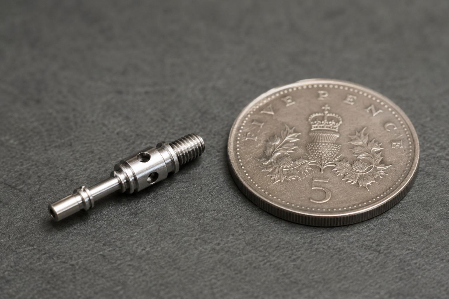 Small precision turned component beside 5p coin